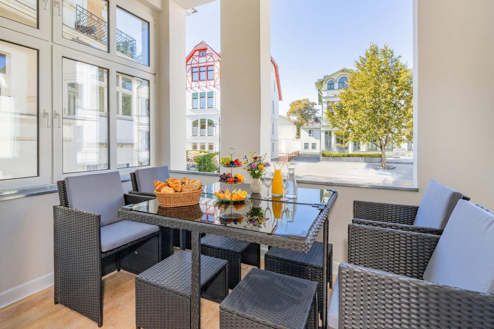 Terrasse mit Esstisch, Stühlen und Frühstück. Blick auf Gebäude und Baum.
