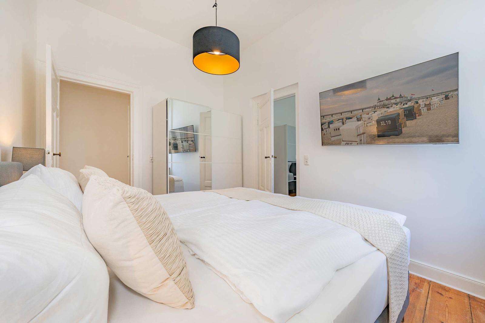 Schlafzimmer mit Bett, Wandbild und Deckenleuchte.
