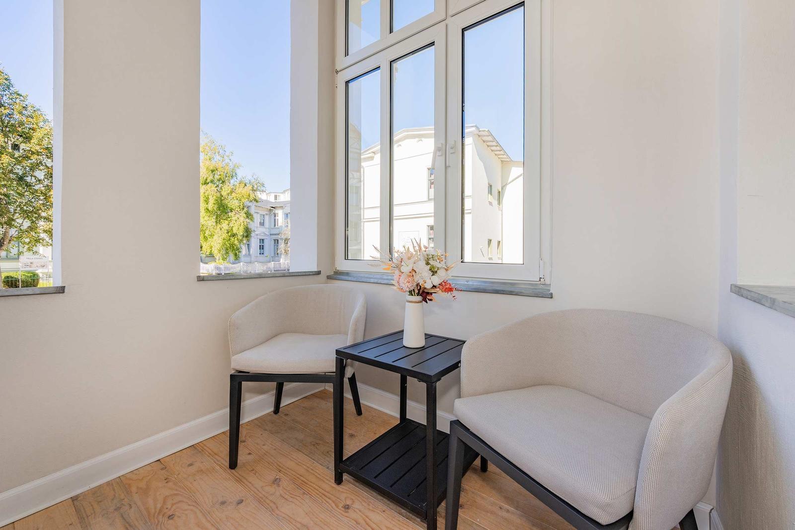 Zwei Sessel und ein Tisch stehen vor einem großen Fenster mit Blick auf Gebäude.