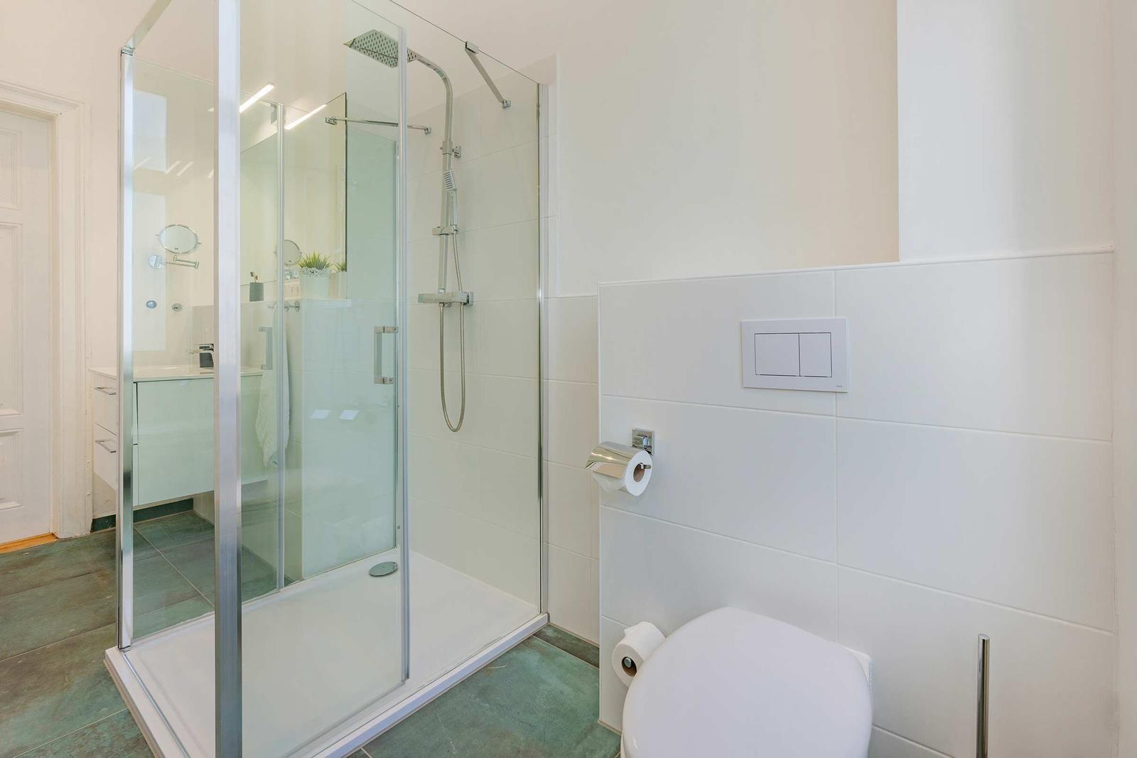 Badezimmer mit Dusche, Toilette und Waschbecken. Fliesenwand und Glasdusche.