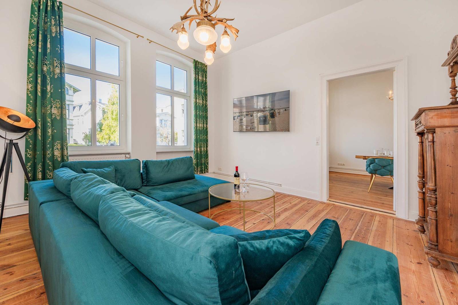 Ein Wohnzimmer mit grünem Sofa, Holzboden und großen Fenstern.