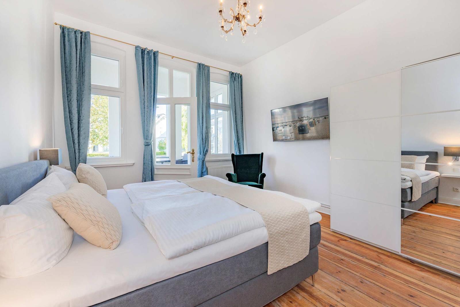 Schlafzimmer mit Doppelbett, blauen Vorhängen und Holzboden. Spiegelwand und Wandbild.