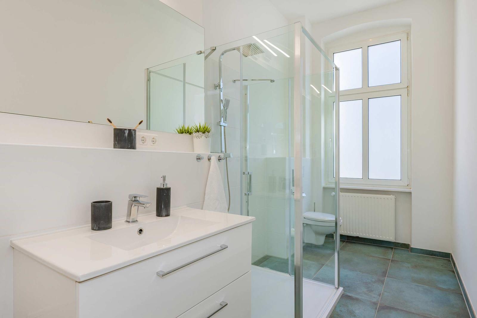 Bad mit Dusche, Waschbecken und Toilette. Fenster mit Heizkörper darunter.