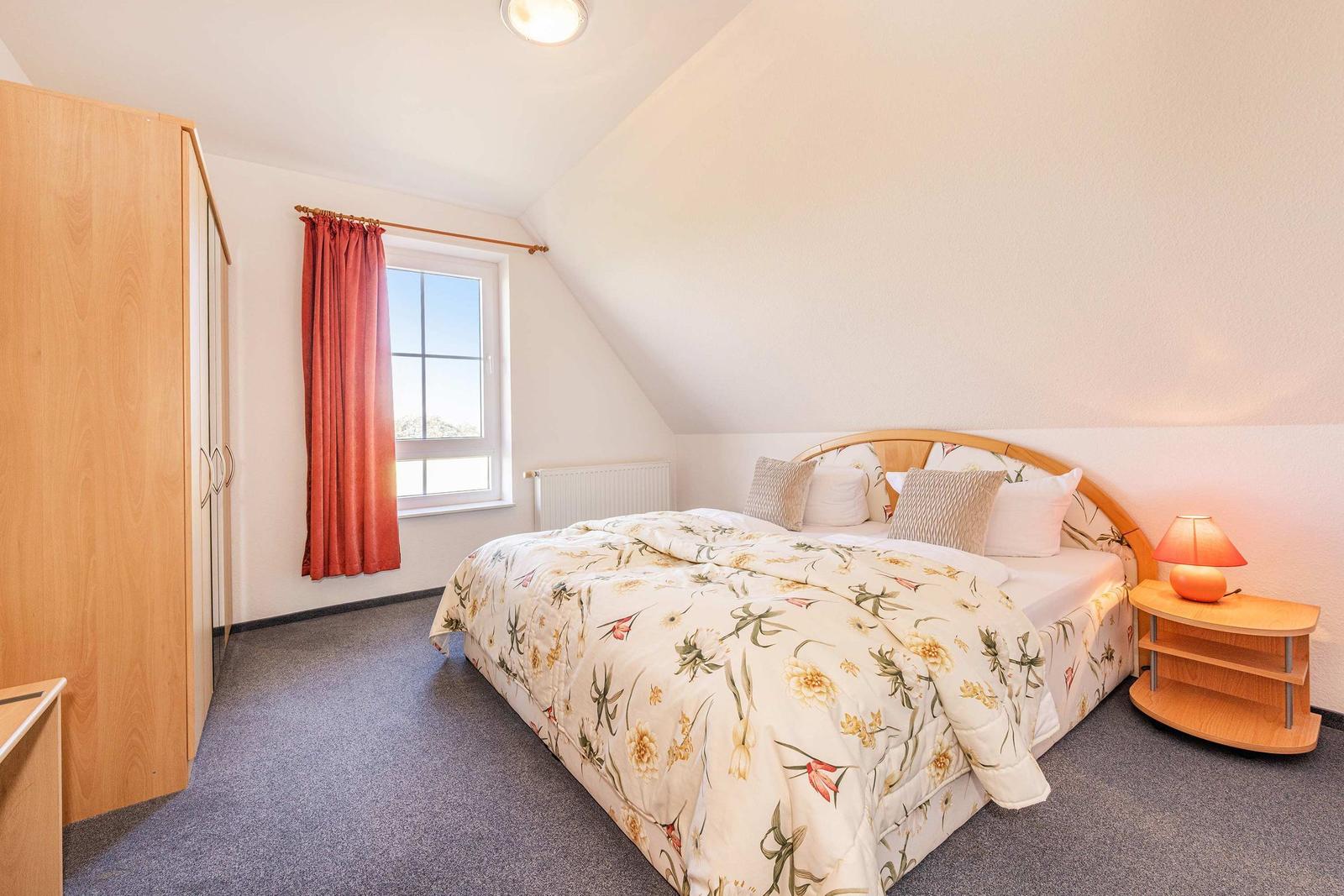 Schlafzimmer mit Bett, Nachttisch, Kleiderschrank und Fenster mit Vorhang.