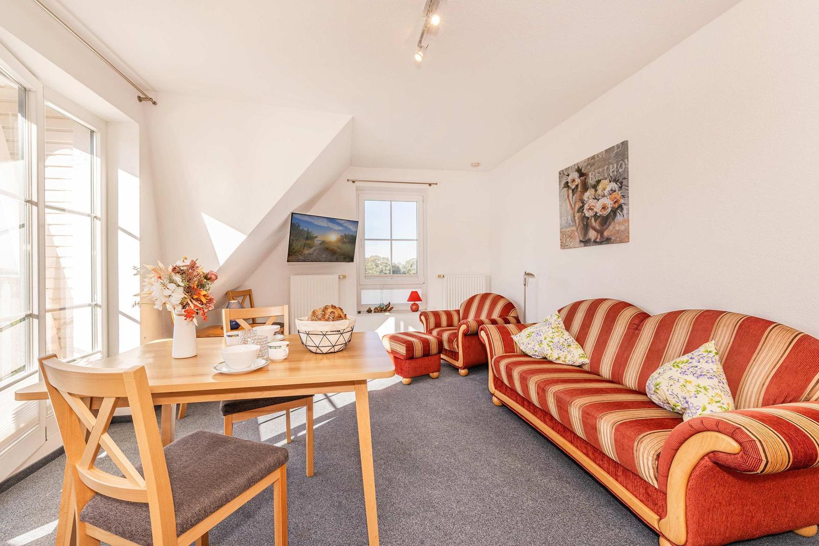 Wohn- und Essbereich mit Sofa, Stühlen und Fenster. Wandbild und TV sichtbar.
