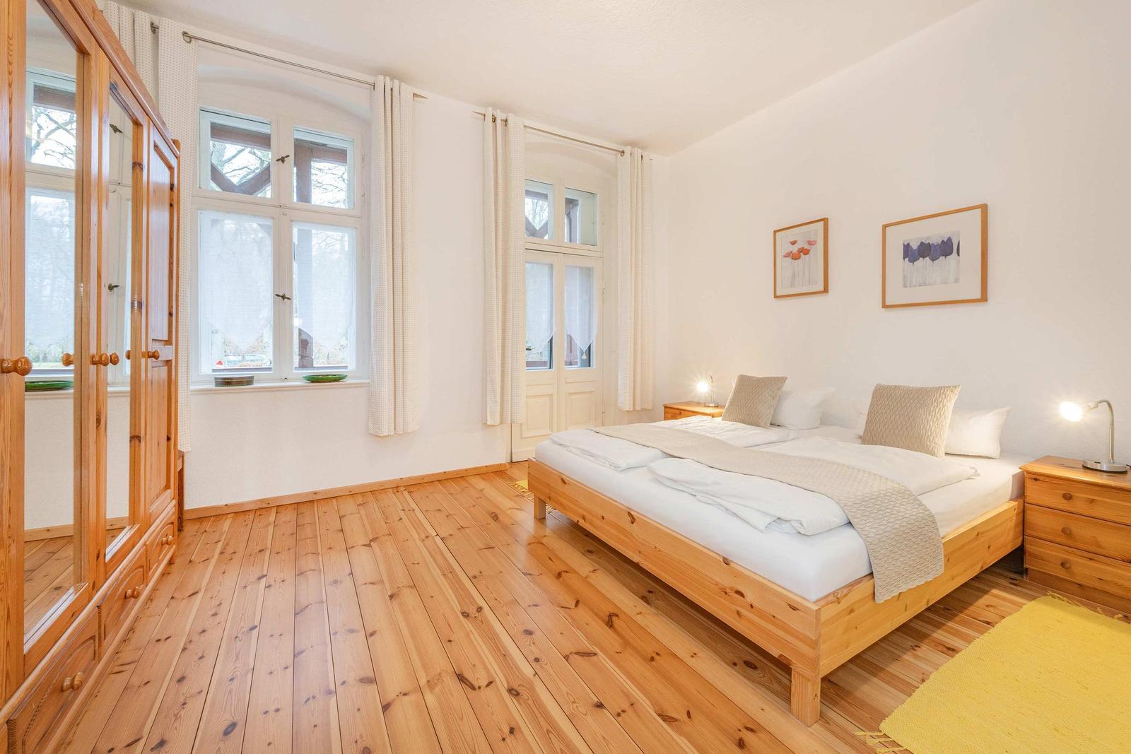 Schlafzimmer mit Holzboden, Bett, Schrank und Fenstern.