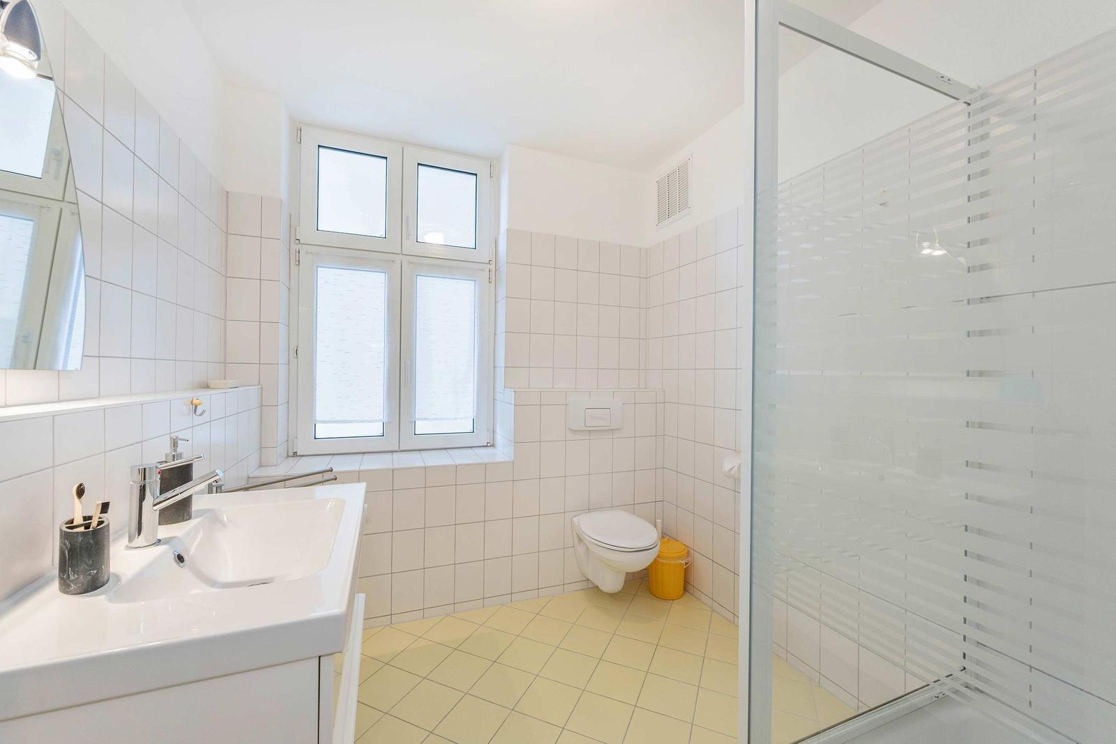 Badezimmer mit Dusche, Waschbecken und Toilette. Fenster mit Milchglas.