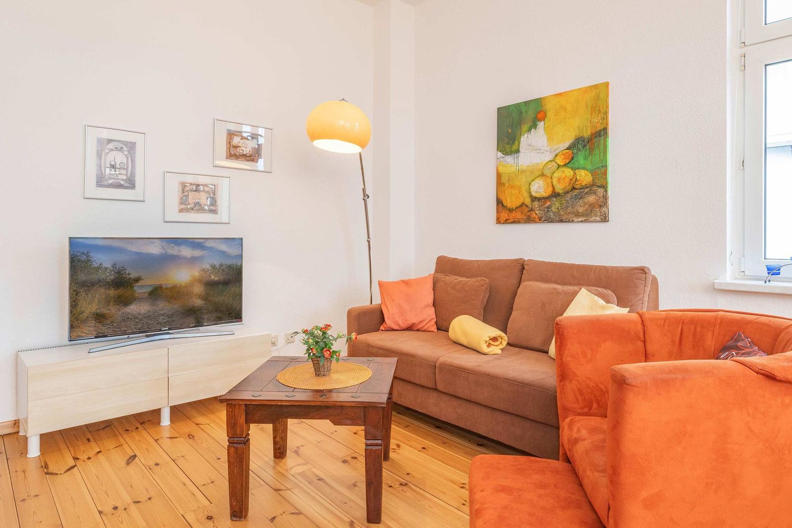 Wohnzimmer mit Sofa, Couchtisch und Fernseher. Holzboden und Wandbilder.