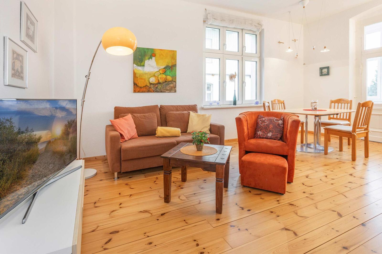 Wohnzimmer mit Sofa, Sessel und Esstisch. Holzboden und große Fenster.