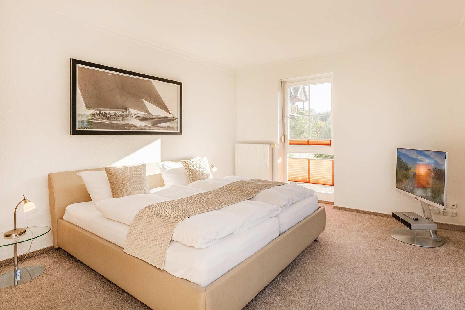 Schlafzimmer mit Bett, Fernseher und Fenster zur Außenterrasse.