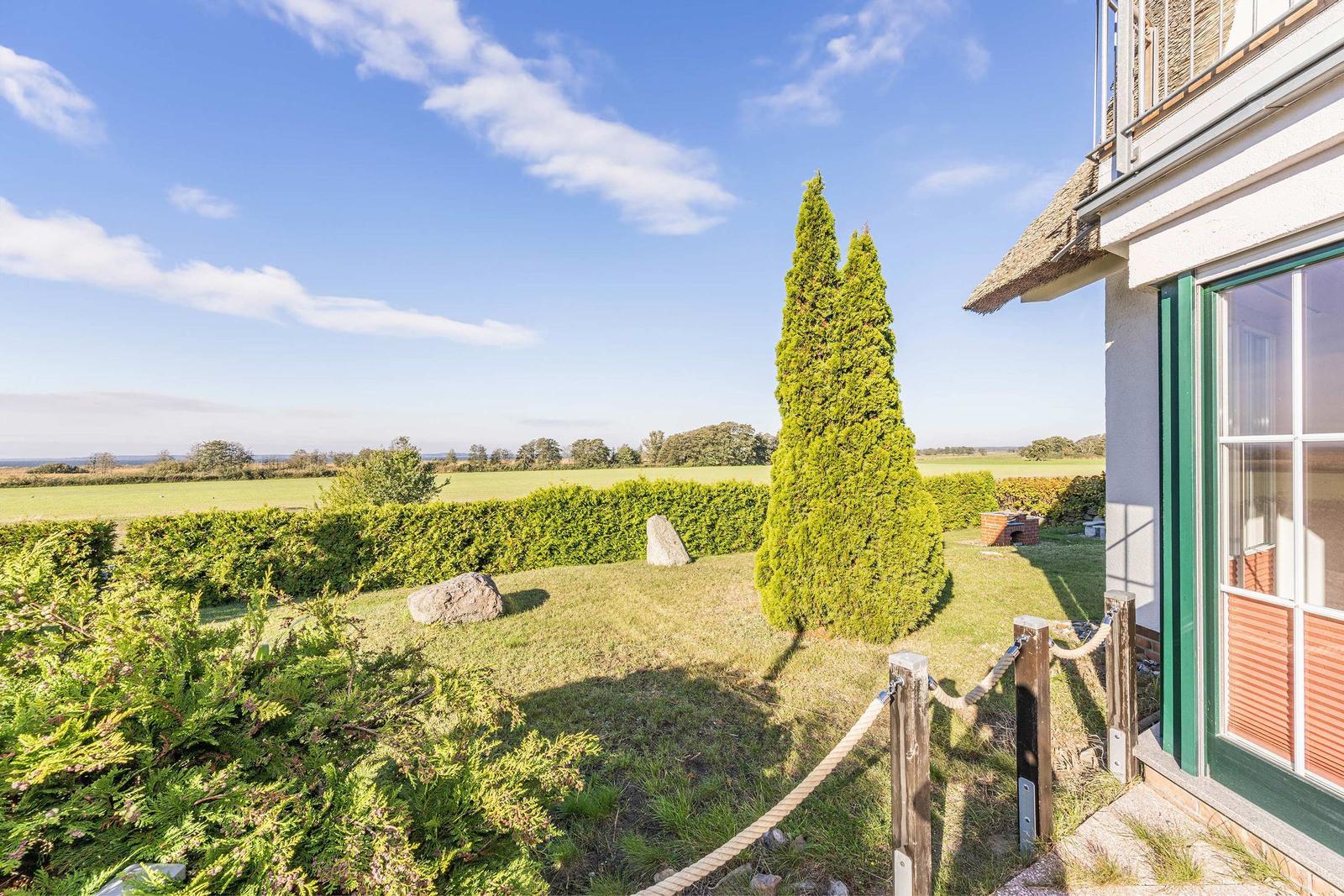 Haus mit Garten, Blick auf Felder und Himmel. Hoher Zypressebaum und Stein im Vorgarten.