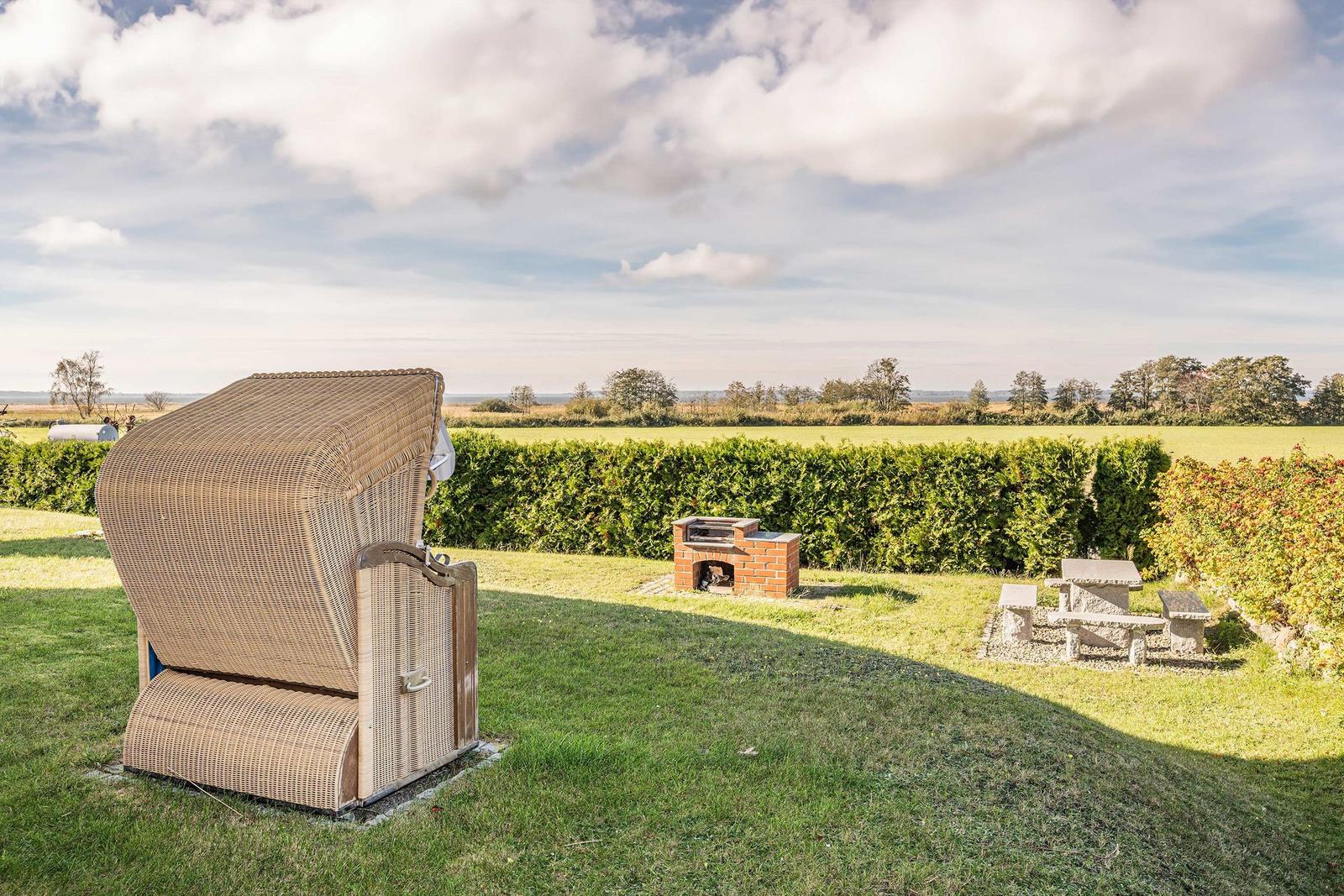 Rattanliege, Grill und Tisch im Garten mit Blick auf Felder.