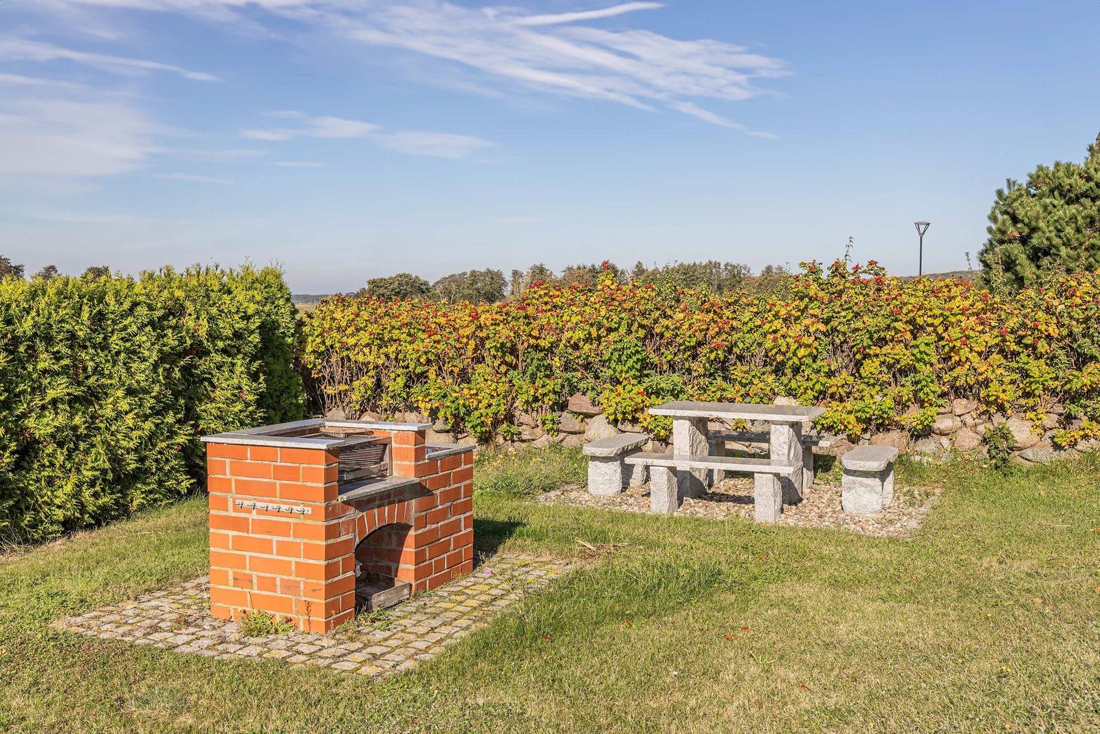 Roter Backstein-Grill und Steinbank im Garten mit Hecken und Gras.
