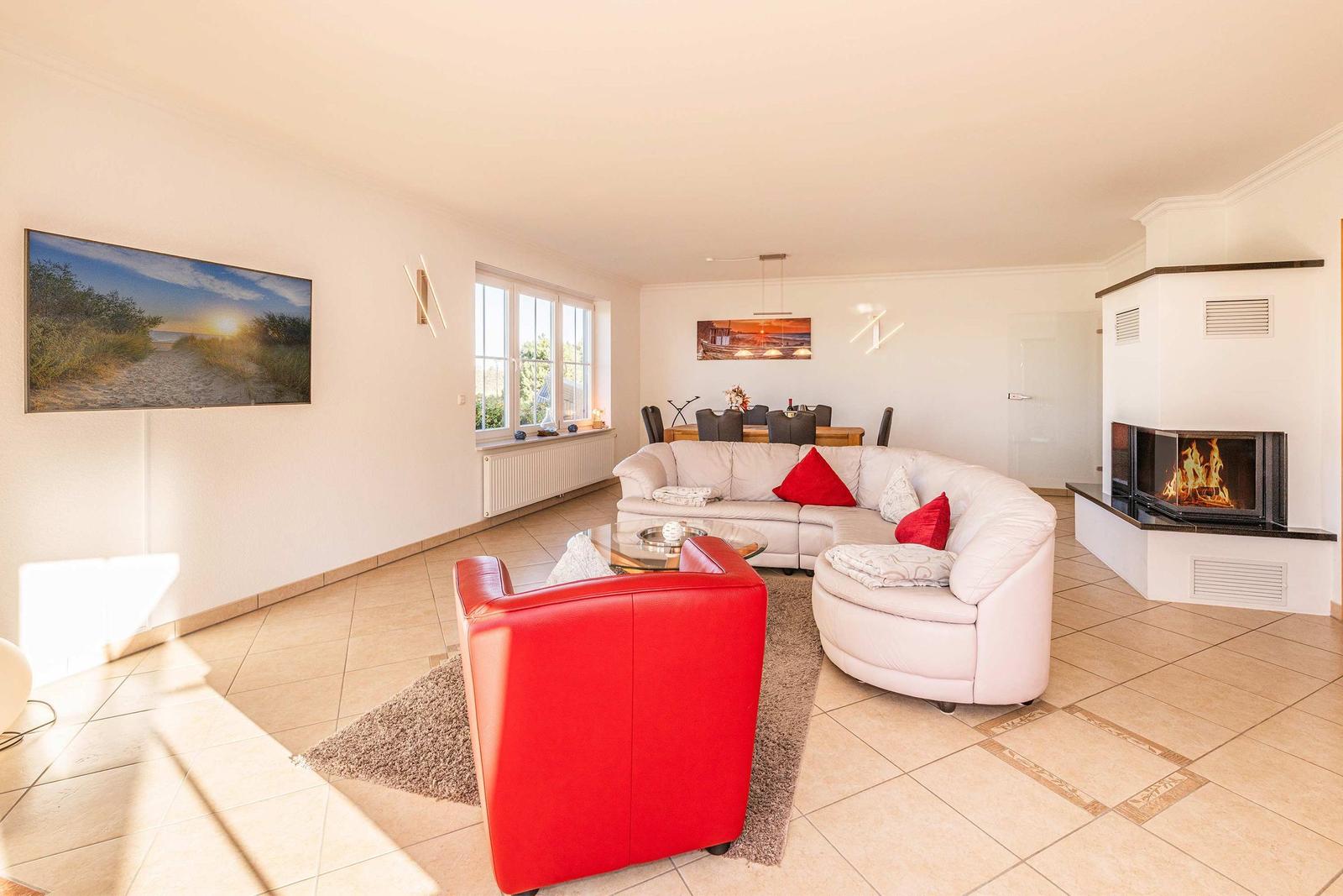Wohnzimmer mit rotem Sessel, weißem Sofa und Kamin mit brennendem Feuer.