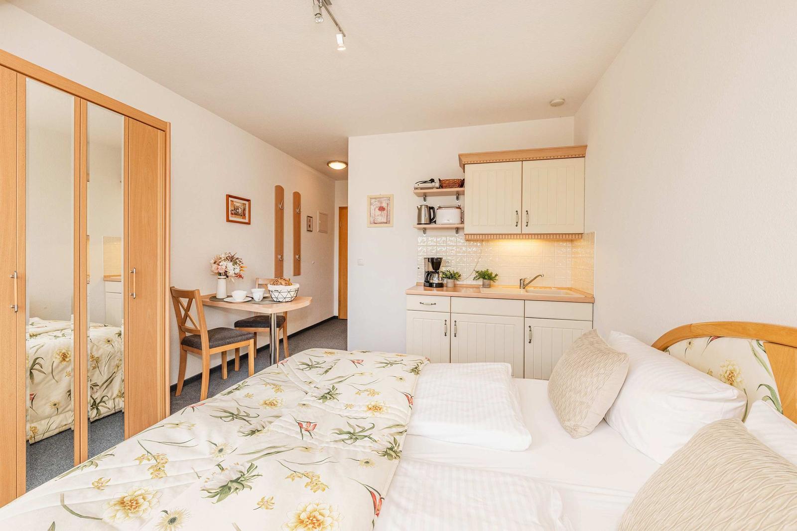 Schlafzimmer mit kleiner Küche und Esstisch. Spiegelwand und Bett mit Blumenbezug.