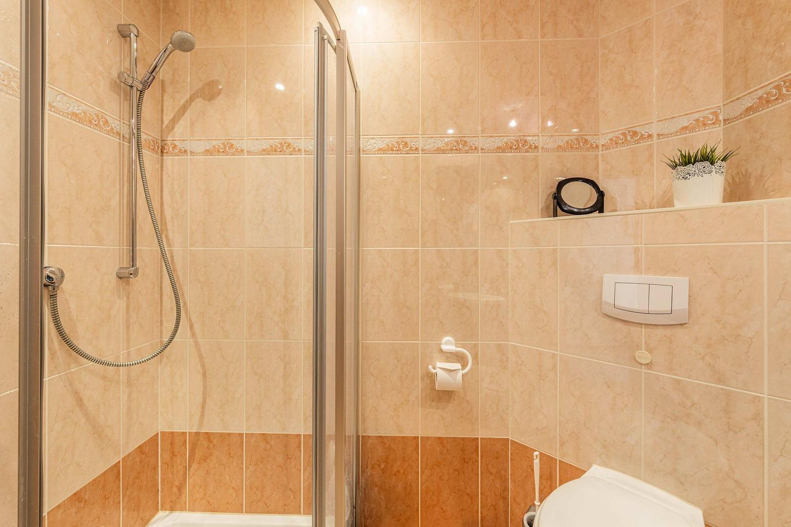 Bad mit Dusche, Toilette und Toilettenpapierhalter an der Wand.
