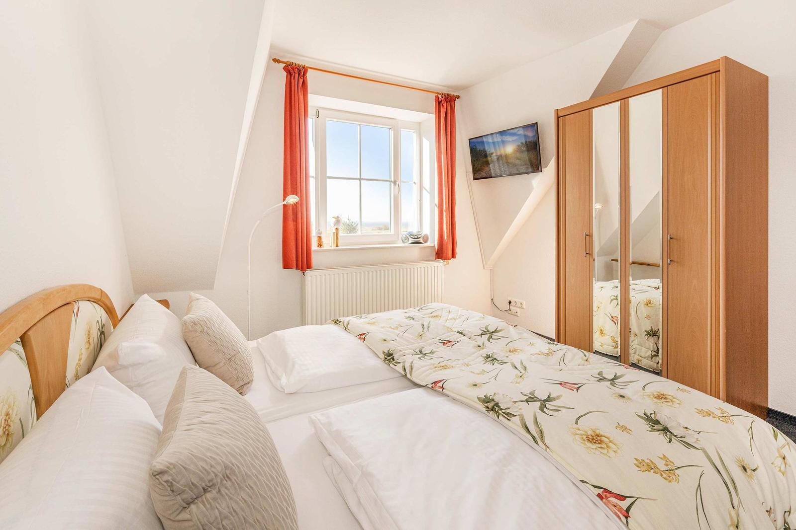 Schlafzimmer mit Doppelbett, Fenster mit roten Vorhängen und Spiegelschrank.