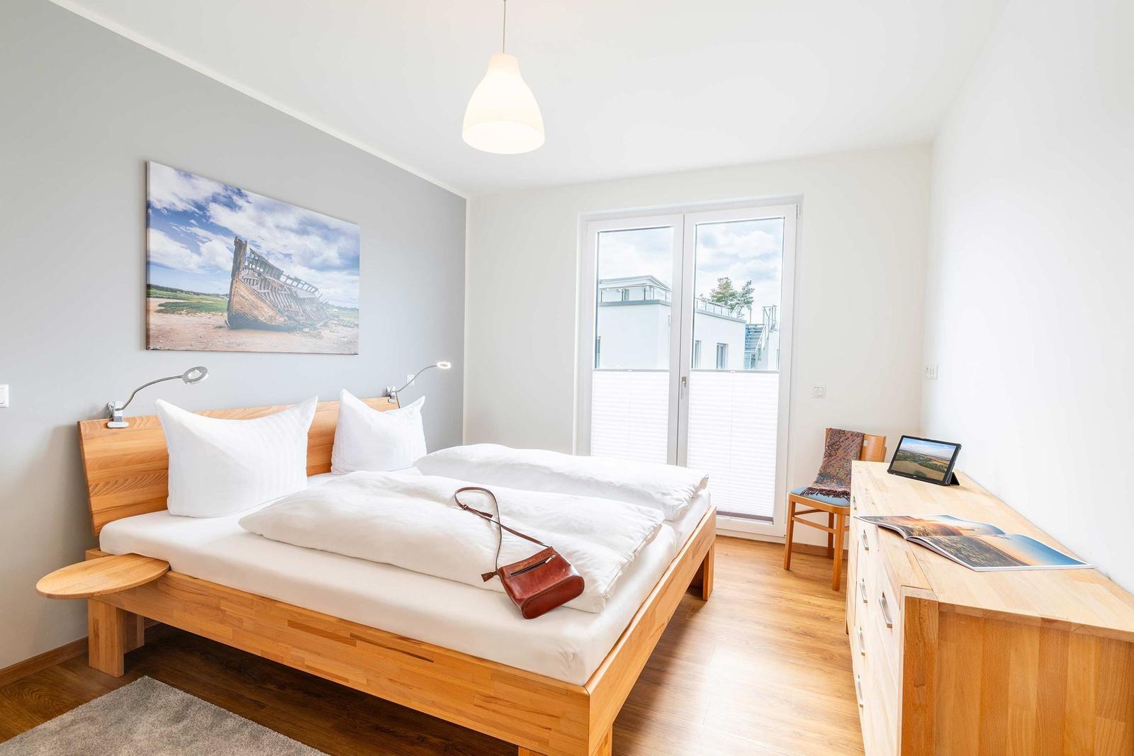 Schlafzimmer mit Holzbett, Fenster und Schreibtisch.