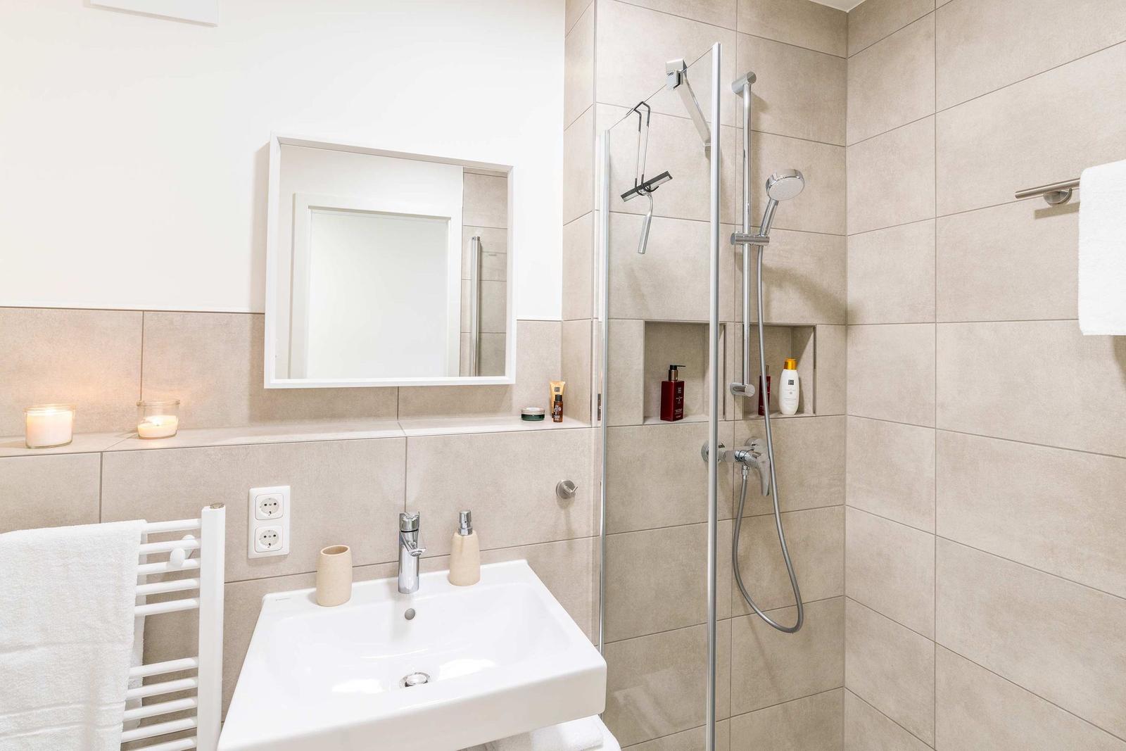 Bad mit Dusche, Waschbecken und Spiegel. Handtuchhalter und Kerzen sind sichtbar.