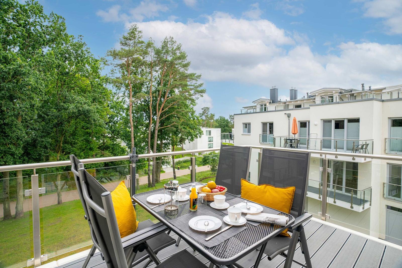 Terrasse mit Tisch, Stühlen und gelben Kissen. Blick auf Grün und moderne Gebäude.