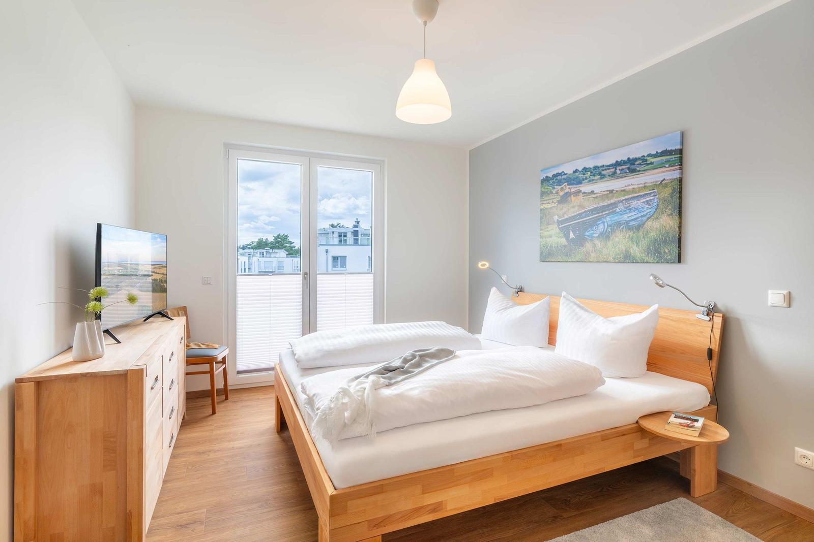 Schlafzimmer mit Bett, TV und Fenster zum Balkon