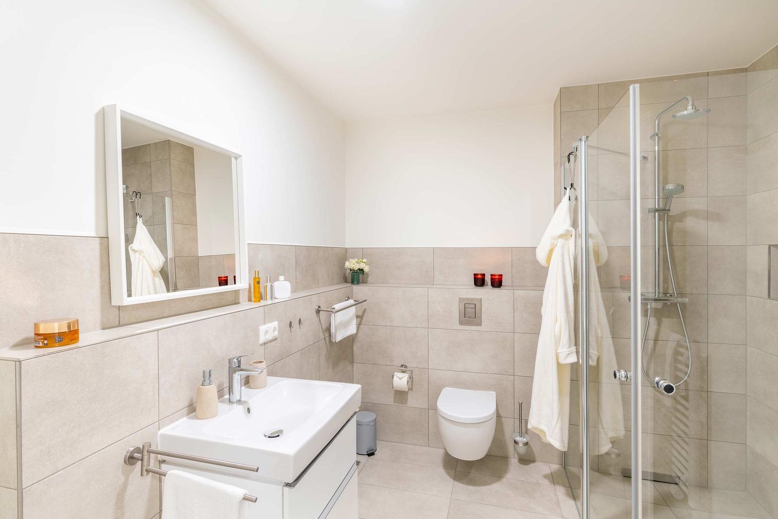 Badezimmer mit Dusche, Waschbecken und Toilette. Weiße Fliesen und moderne Einrichtung.