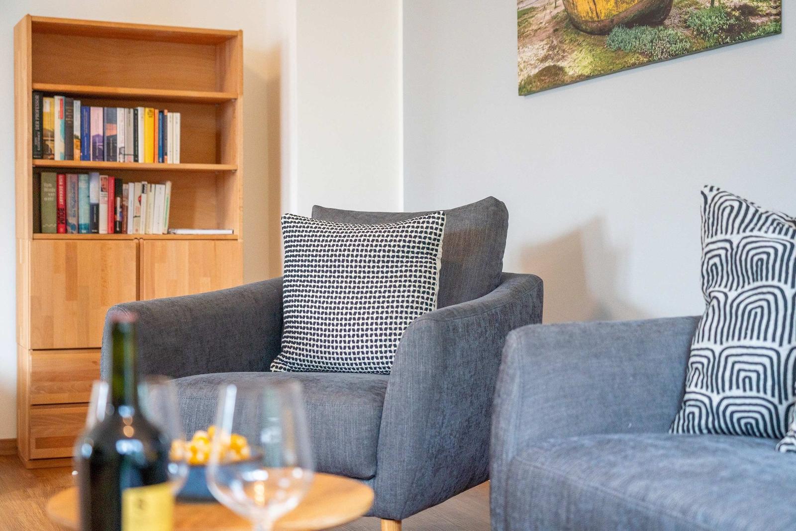 Zwei graue Sessel mit Kissen, Bücherregal und Wandbild im Wohnbereich.