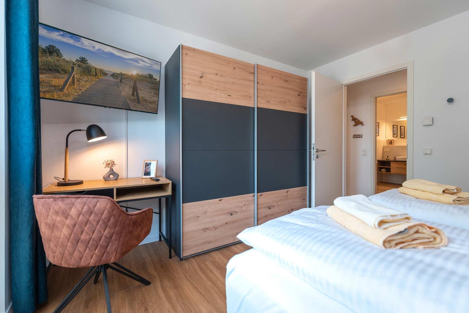 Schlafzimmer mit Bett, Schrank und Schreibtisch mit Lampe und Bild