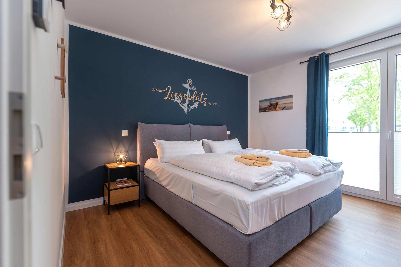 Schlafzimmer mit Bett, dunkelblauer Wand und Blick auf Balkon.