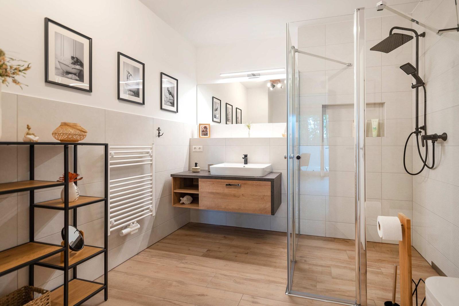 Badezimmer mit Dusche, Waschbecken und Regal. Holzboden und Wandfliesen.