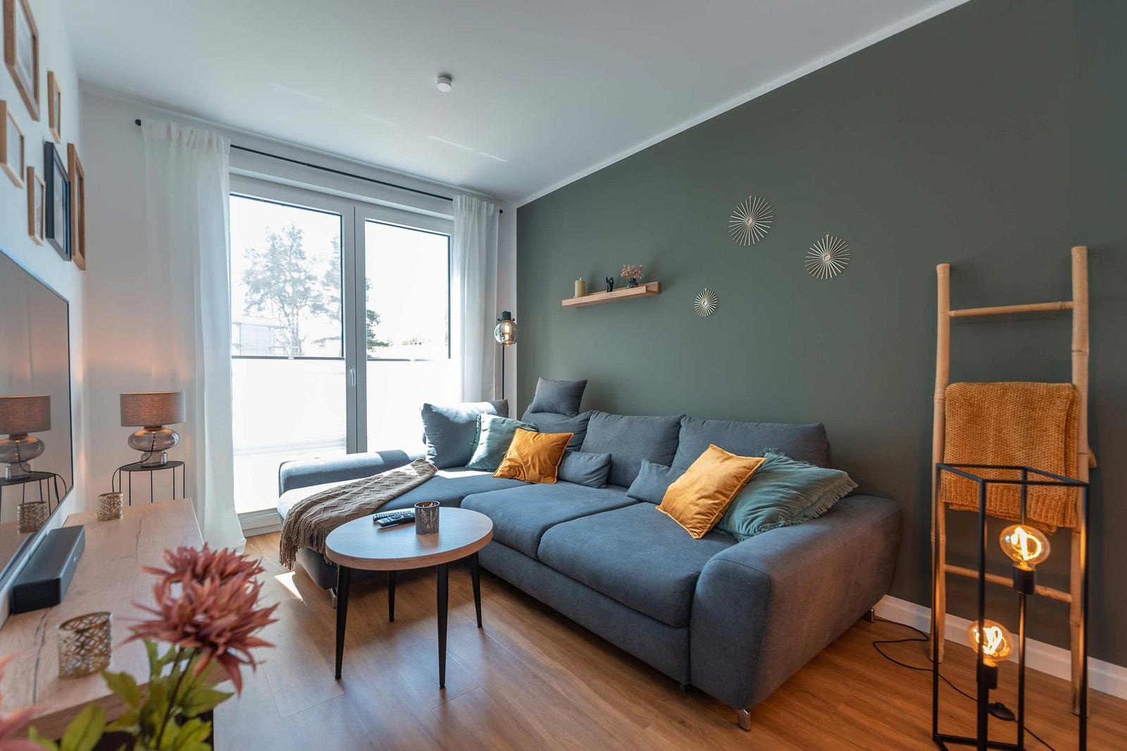 Ein Wohnzimmer mit grauem Sofa, Holzboden und großen Fenstern.