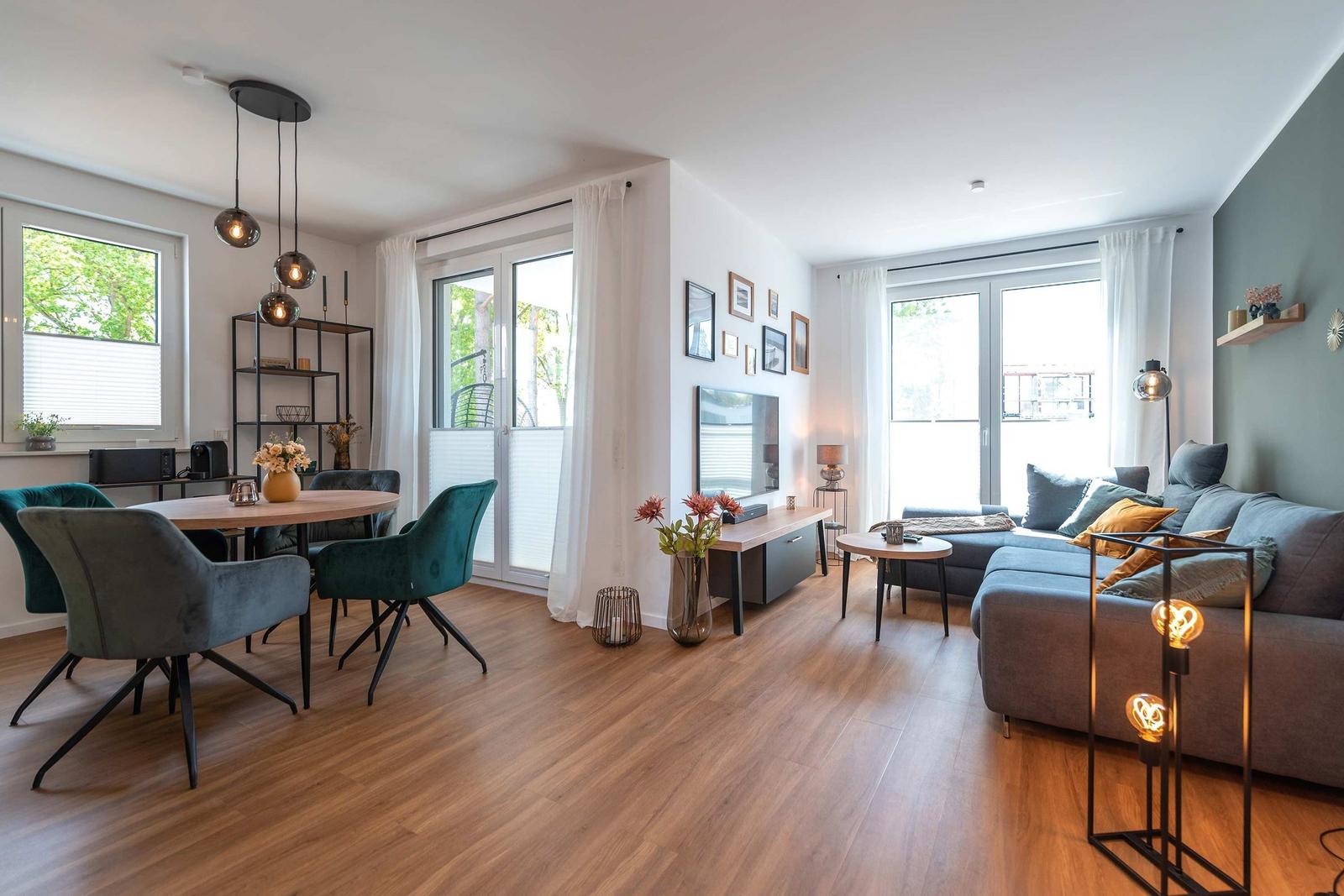 Wohn- und Essbereich mit Holzboden, Sofa, Esstisch und Fenstern.