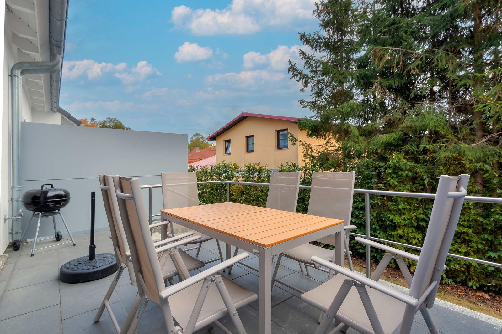 Terrasse mit Tisch, Stühlen und Grill. Blick auf Haus und Bäume.