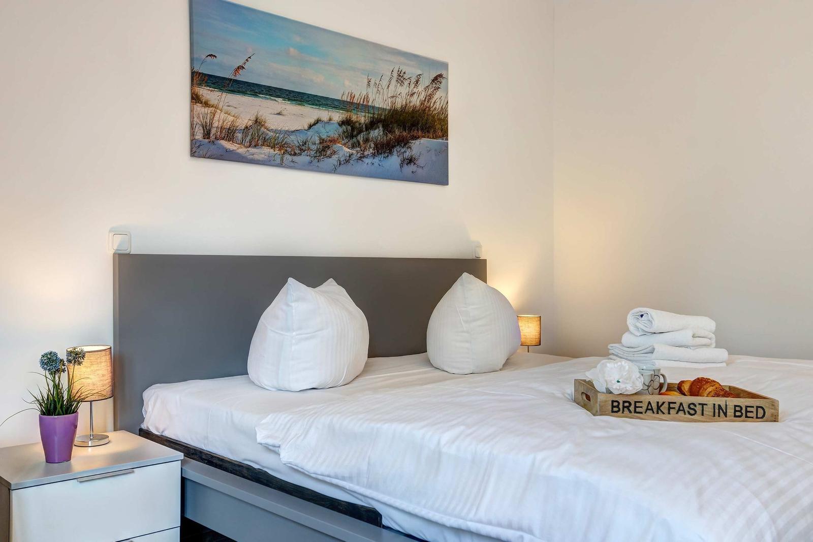 Doppelbett mit weißer Bettwäsche, Kissen und Frühstückstablett.