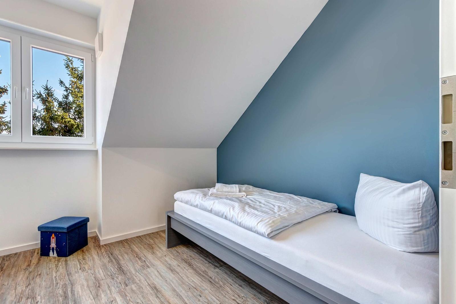 Schlafzimmer mit Dachschrägen, Bett und Fenster mit Blick auf Bäume.