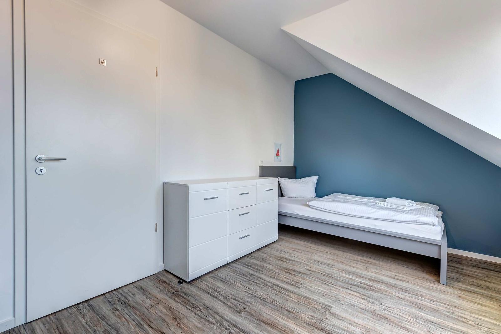 Schlafzimmer mit Doppelbett, Schrank und Holzboden unter Dachschräge.