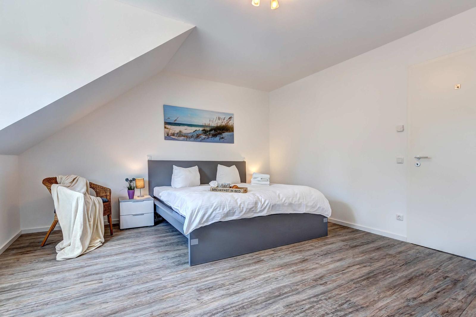 Schlafzimmer mit Dachschräge, Bett, Nachttisch und Stuhl.