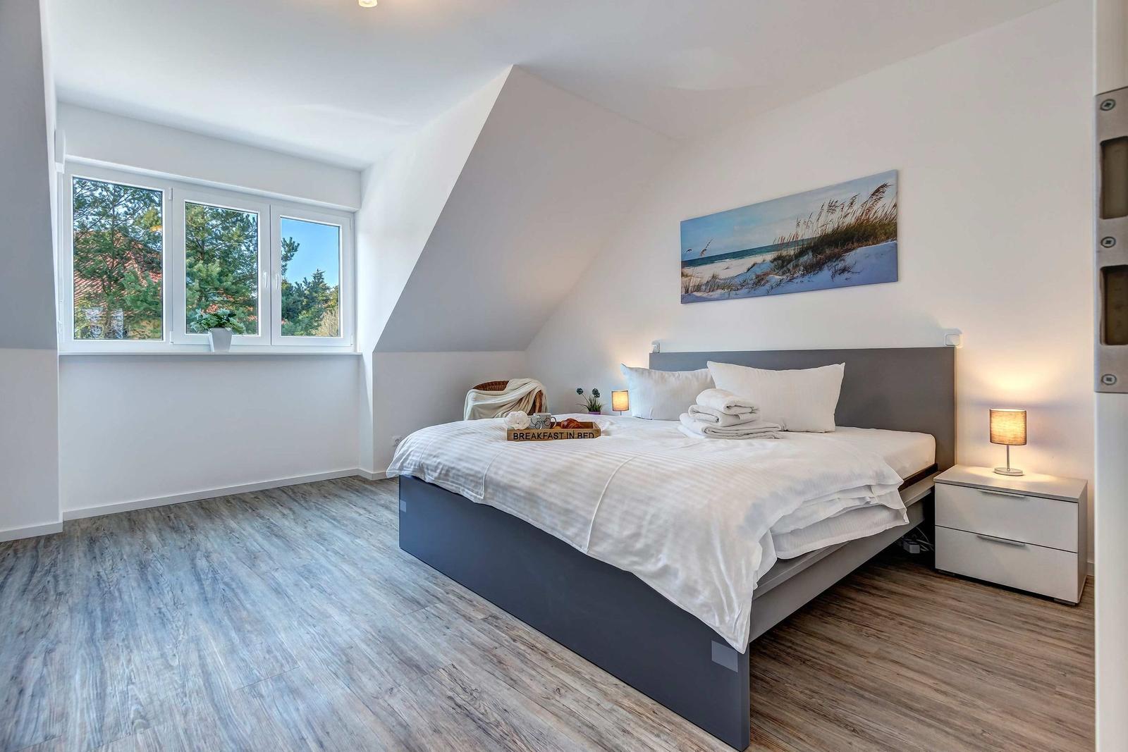 Schlafzimmer mit Dachschrägen, großem Bett und Fenster mit Blick auf Bäume.