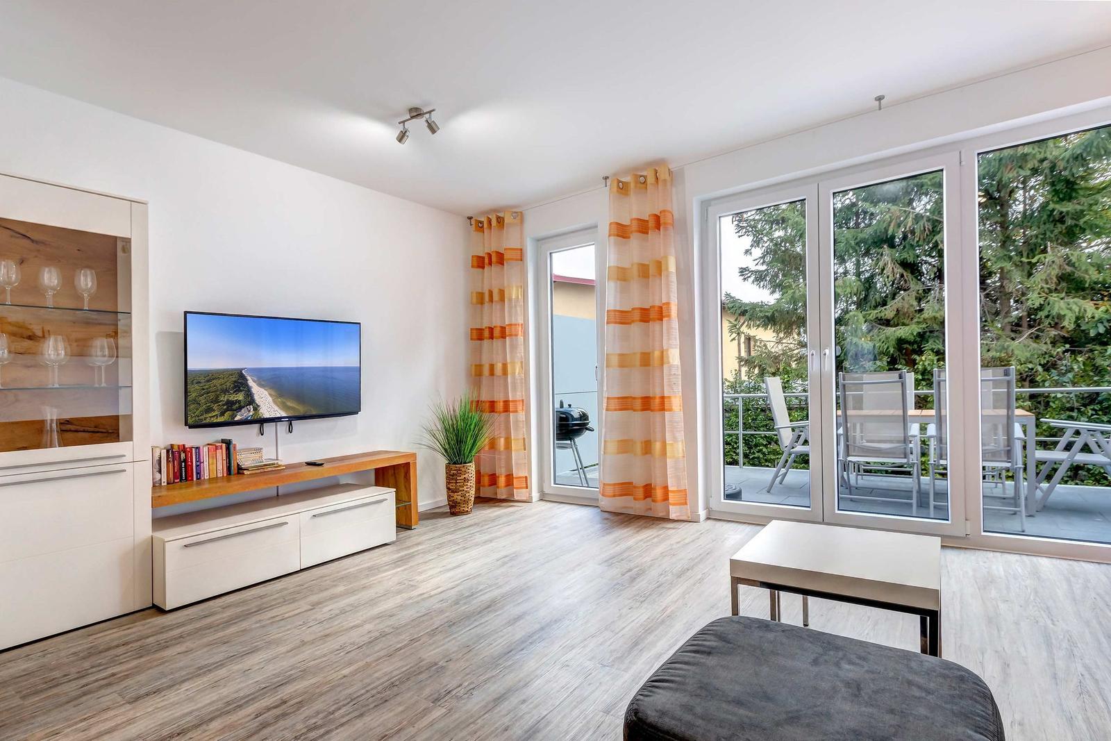 Wohnzimmer mit TV, Terrasse und Balkon. Holzfußboden und orange-gestreifte Vorhänge.