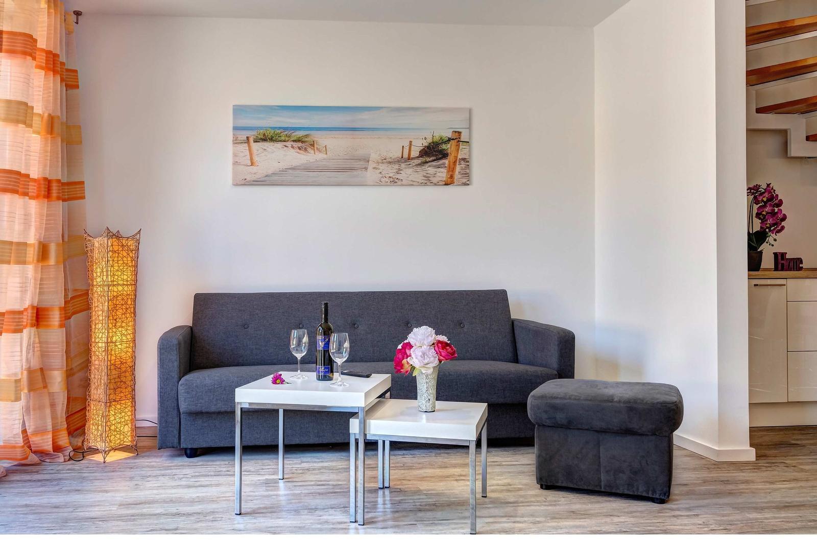 Ein Wohnzimmer mit grauem Sofa, zwei weißen Tischen und einer Wanddekoration.