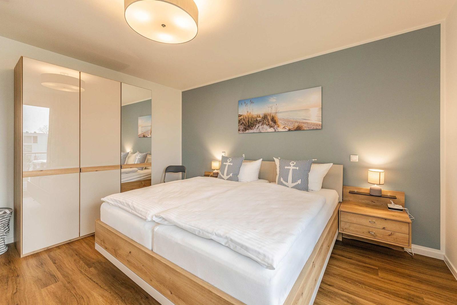 Bedroom with double bed, wooden furniture, and wall art. Mirror wall and nightstands.