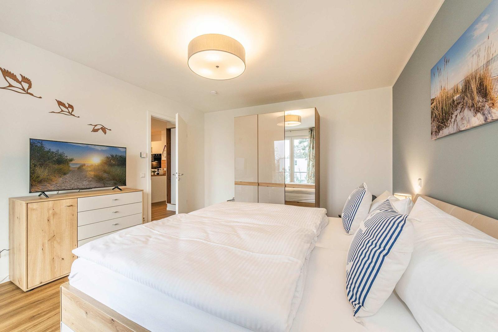 Bedroom with double bed, TV, and wardrobe. Wall art and wooden furniture.