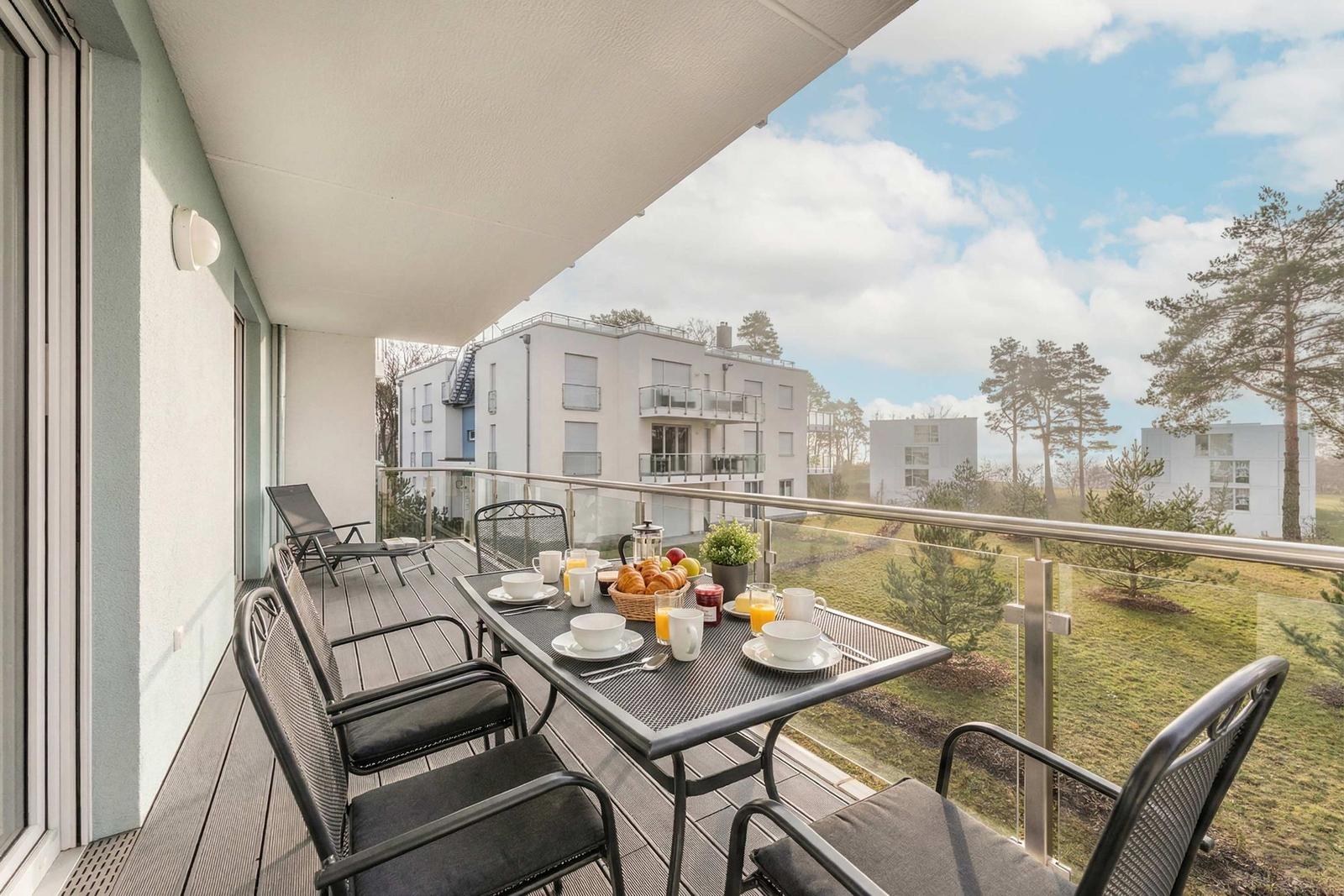 Terrace with table, chairs, and breakfast. View of apartment buildings and trees.