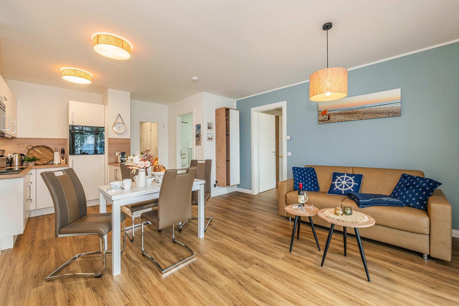 Living and dining area with sofa, dining table, and kitchen. Wooden floor and blue wall.
