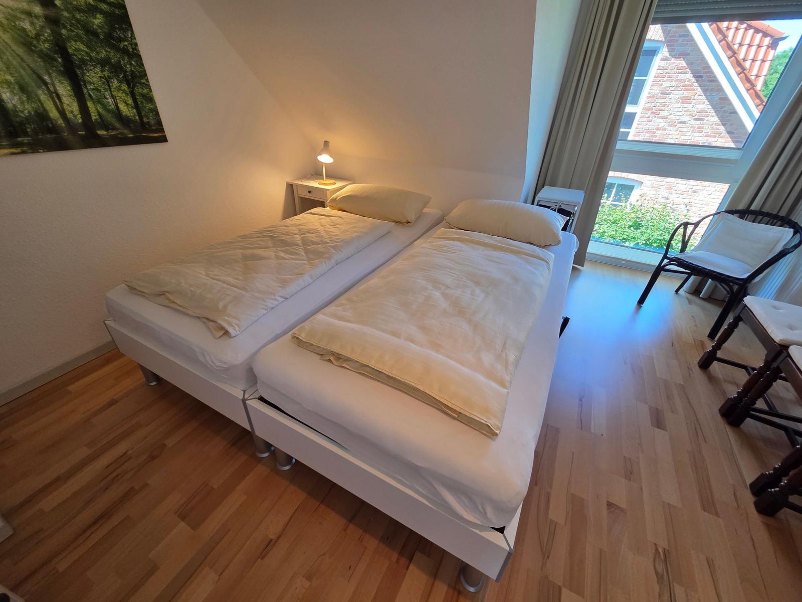 Zwei Einzelbetten mit weißen Bettwäschen stehen im Raum mit Holzboden und großem Fenster.