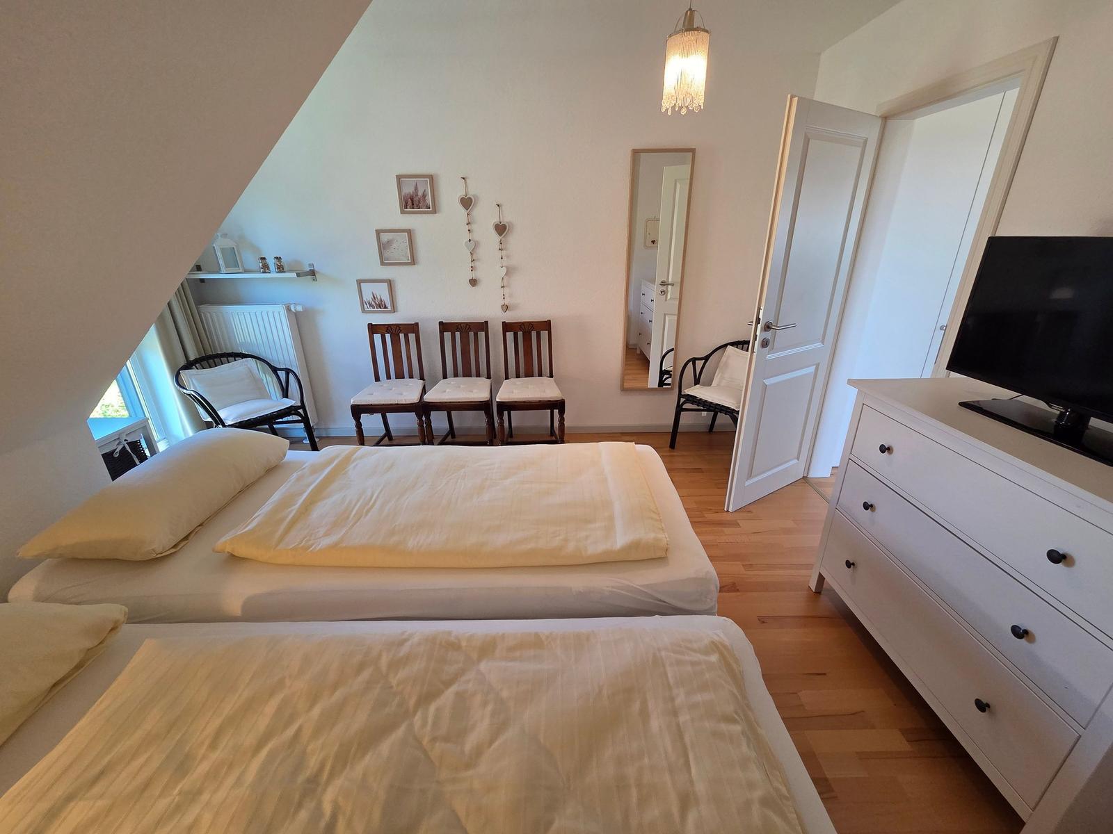 Zwei Betten, Schreibtisch, Fernseher und Spiegel in einem Schlafzimmer mit Holzboden und Dachschrägen.