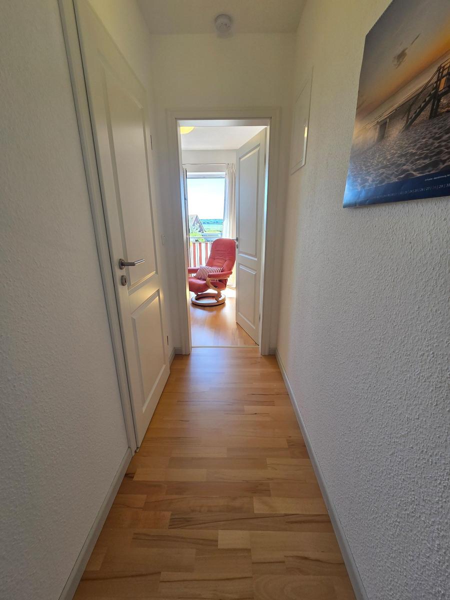 Flur mit Holzboden führt zu einem Raum mit rotem Sessel und Balkon.