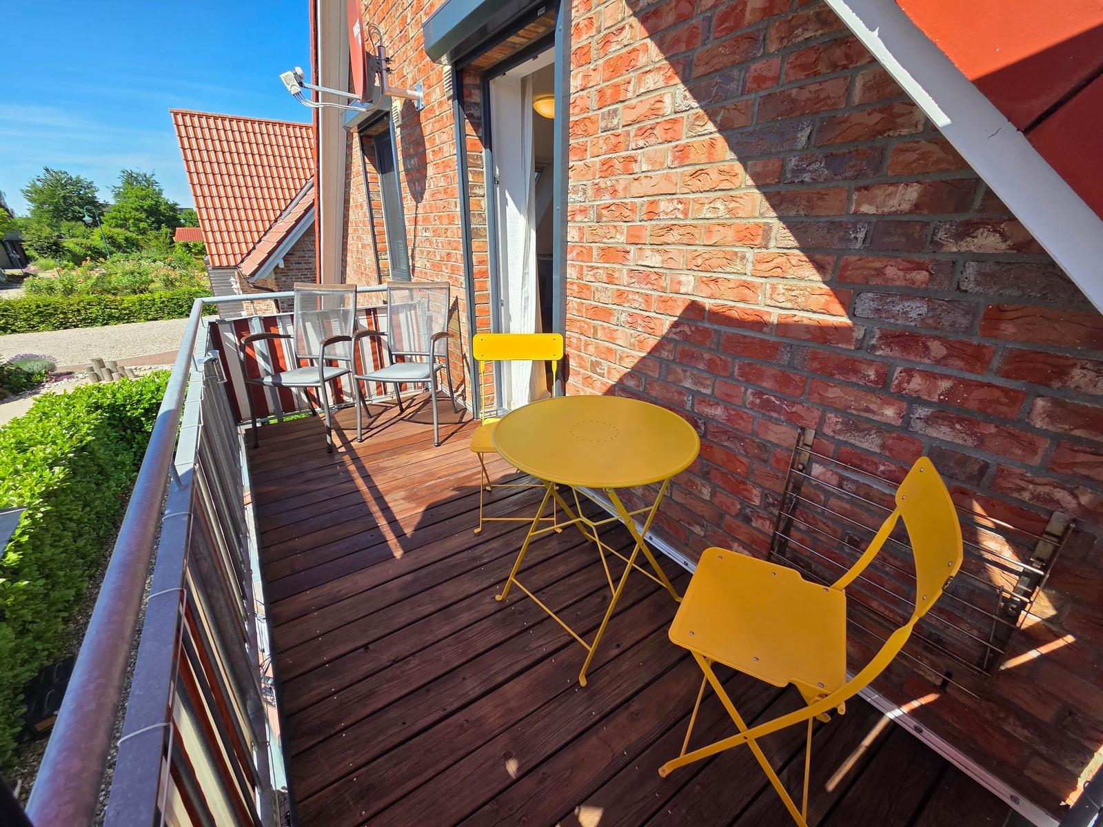 Terrasse mit gelbem Tisch und Stühlen, Holzboden, roter Backsteinwand und Gartenblick.
