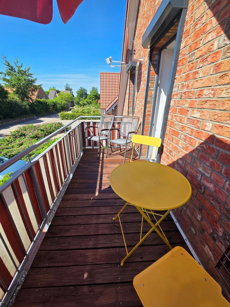 Terrasse mit gelbem Tisch und Stühlen, roter Backsteinwand und Blick auf grüne Umgebung.