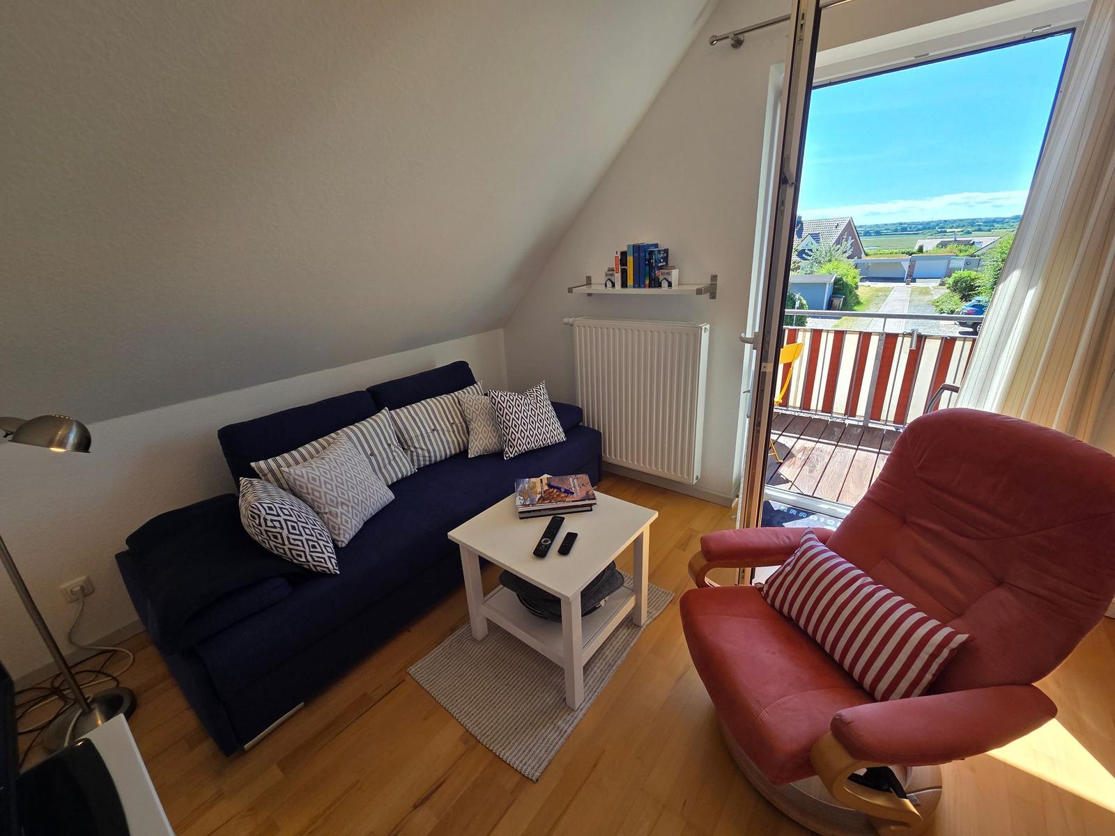 Ein Wohnzimmer mit Sofa, Sessel und Balkonansicht.